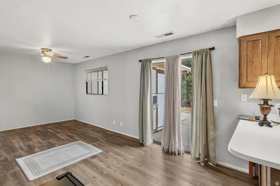 Wood-finish flooring, ceiling fan with integrated lighting, window with horizontal muntins, sliding glass door, and upper cabinetry