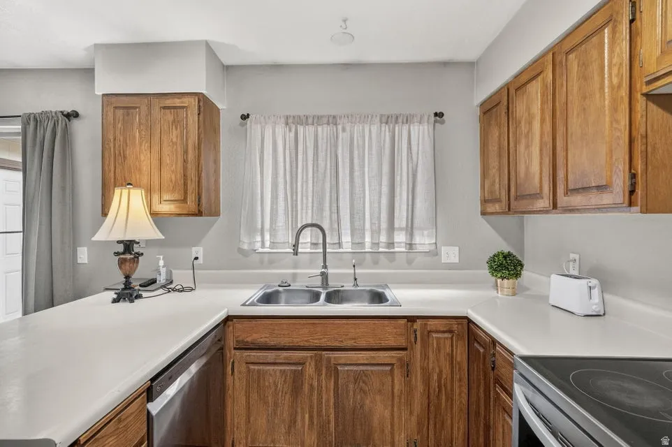 Wood-finish cabinetry, stainless steel double basin sink with gooseneck faucet, light-toned countertops, and integrated dishwasher