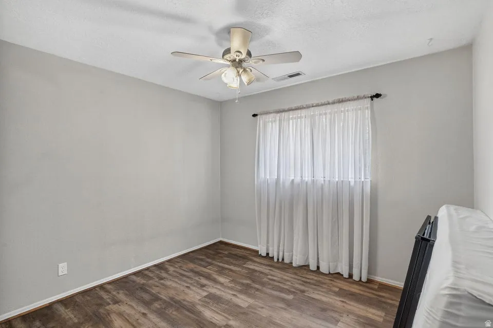 Wood-finish flooring, ceiling fan with integrated lighting, and a window with curtain rod
