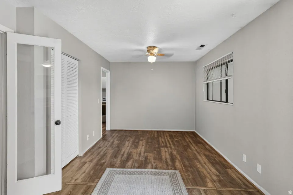 Wood-finish flooring, ceiling fan with integrated lighting, window with blinds, and white bi-fold closet doors