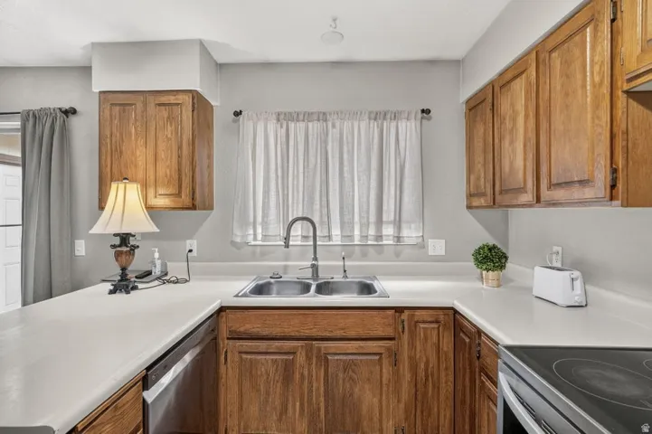 Wood-finish cabinetry, stainless steel double basin sink with gooseneck faucet, light-toned countertops, and integrated dishwasher