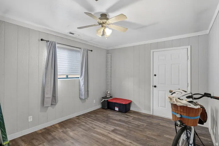 Wood-finish flooring, paneled walls, and a ceiling fan with integrated lighting