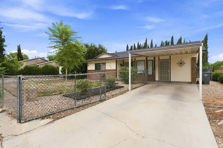 Carport parking, front yard with chain link fencing, concrete driveway, brick accents, and a security screen door
