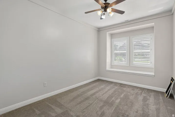 Recessed window with plantation shutters, ceiling fan with integrated lighting, crown molding, and carpeted flooring