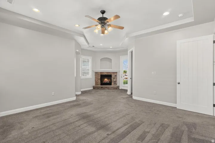 Recessed lighting, ceiling fan, fireplace with stone surround, tray ceiling, and white panel doors