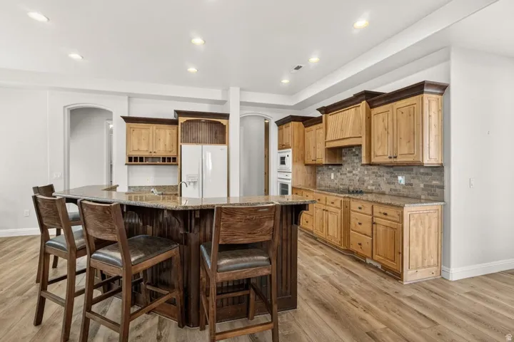 Spacious kitchen featuring an expansive center island, warm wood cabinetry, built-in double ovens, and a neutral tile backsplash