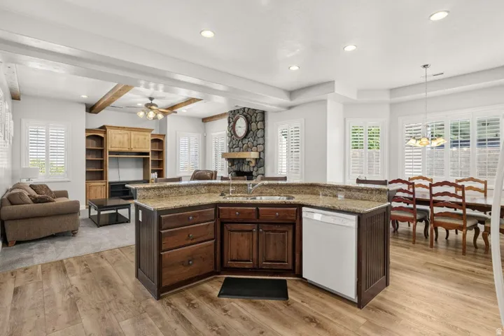 Kitchen island with a built-in sink and dishwasher, wood-finish flooring, built-in entertainment center, stone fireplace, and plantation shutters