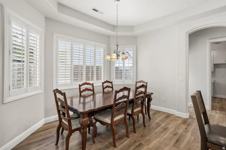Dining area featuring wood-finish flooring, tray ceiling, and white plantation shutters on multiple windows