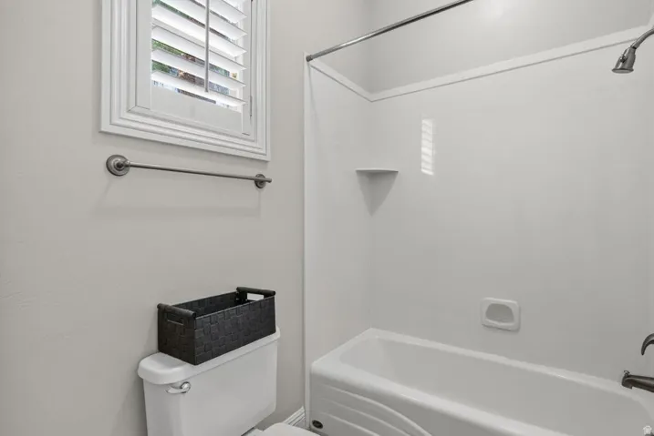 Bathtub with shower, white wall surround, and corner shelf