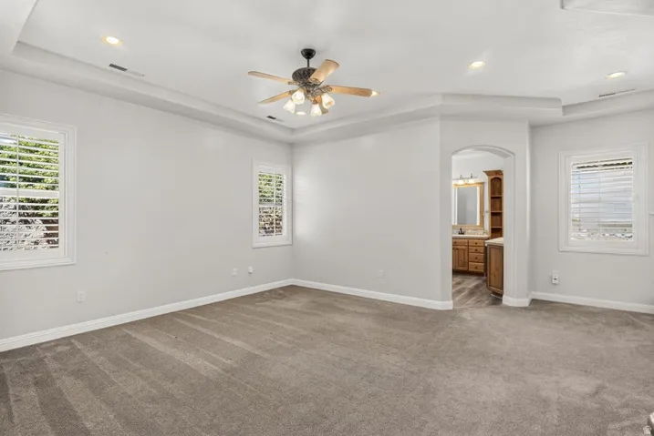 Spacious room featuring tray ceiling, recessed lighting, ceiling fan, and plantation shutters