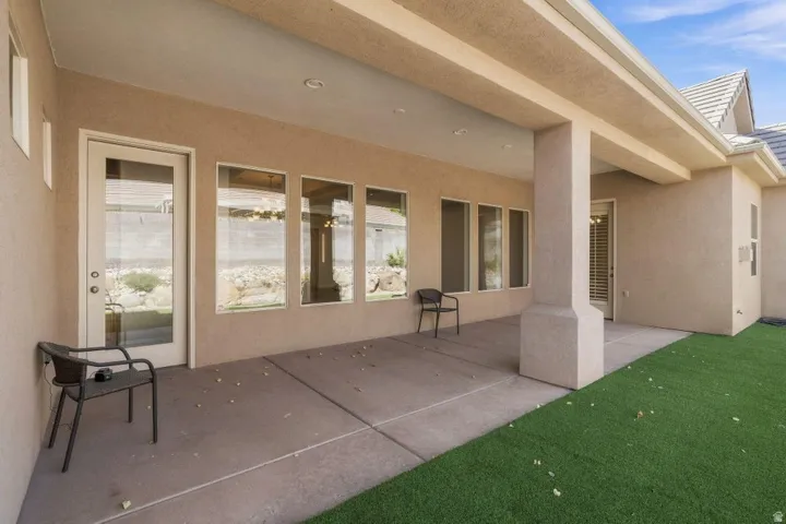 Covered patio with concrete flooring, multiple large windows, and a glass-paneled door