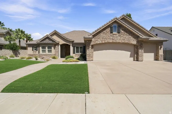 Stucco exterior with stone accents, concrete driveway, arched garage door, and a tiled roof