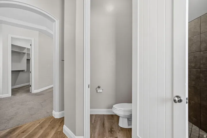 Powder room featuring wood-finish flooring, white toilet, and panel-style door