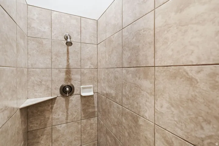 Tiled shower enclosure featuring a corner shelf and a brushed nickel showerhead