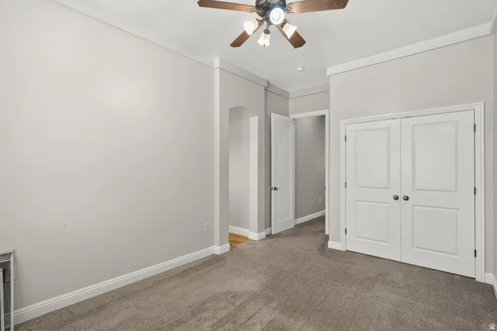 Carpeted flooring, ceiling fan with integrated lighting, white paneled bifold doors, white trim, and a recessed archway