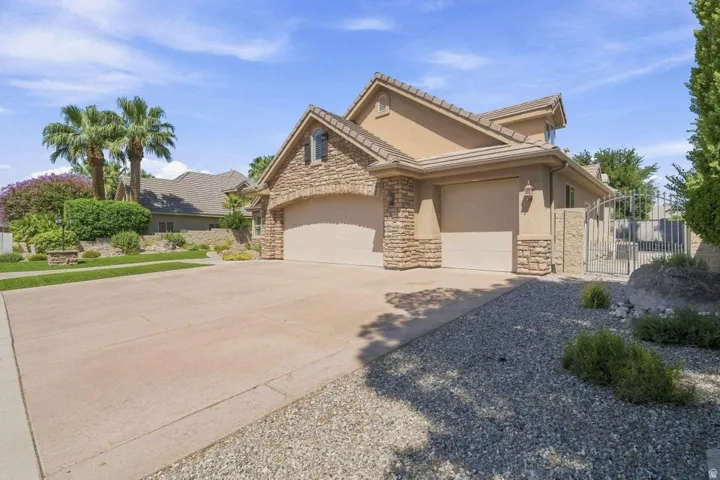 Stucco and stone exterior with a tile roof, featuring a two-car garage, concrete driveway, and decorative wrought iron gate