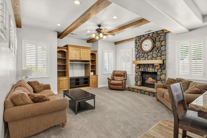 Exposed wood beam ceiling, recessed lighting, ceiling fan, built-in entertainment center, and a stone fireplace with a wood mantle