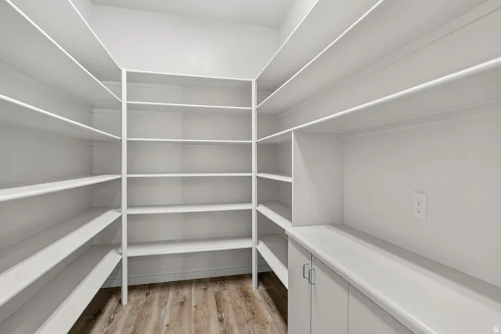 Expansive pantry featuring wrap-around shelving, built-in cabinetry, durable countertops, and wood-finish flooring