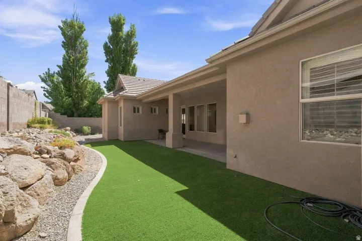 Covered patio area with a stucco exterior, artificial turf, and a rock landscaping bed