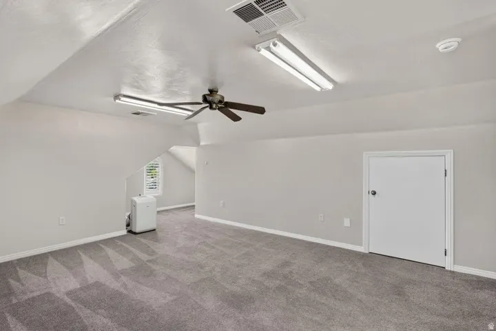 Spacious attic room featuring sloped ceilings, recessed lighting, and a ceiling fan