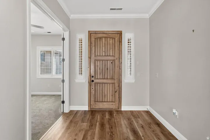 Wood-finish flooring, paneled entry door, vertical sidelight windows, crown molding, and neutral wall tones
