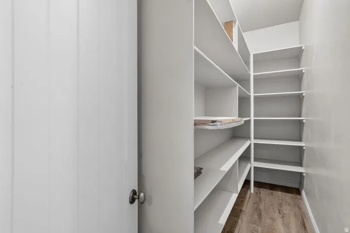 Spacious walk-in pantry with extensive shelving, white painted walls, and wood-finish flooring