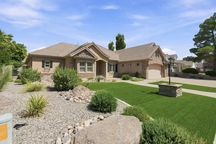 Stucco exterior with stone accents, tile roof, attached two-car garage, and a manicured artificial turf lawn