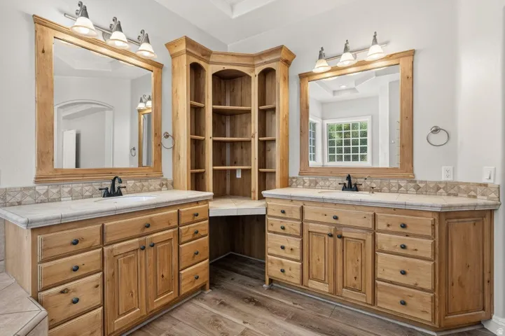Dual wood-finish vanities with undermount sinks, tile countertops, and framed mirrors