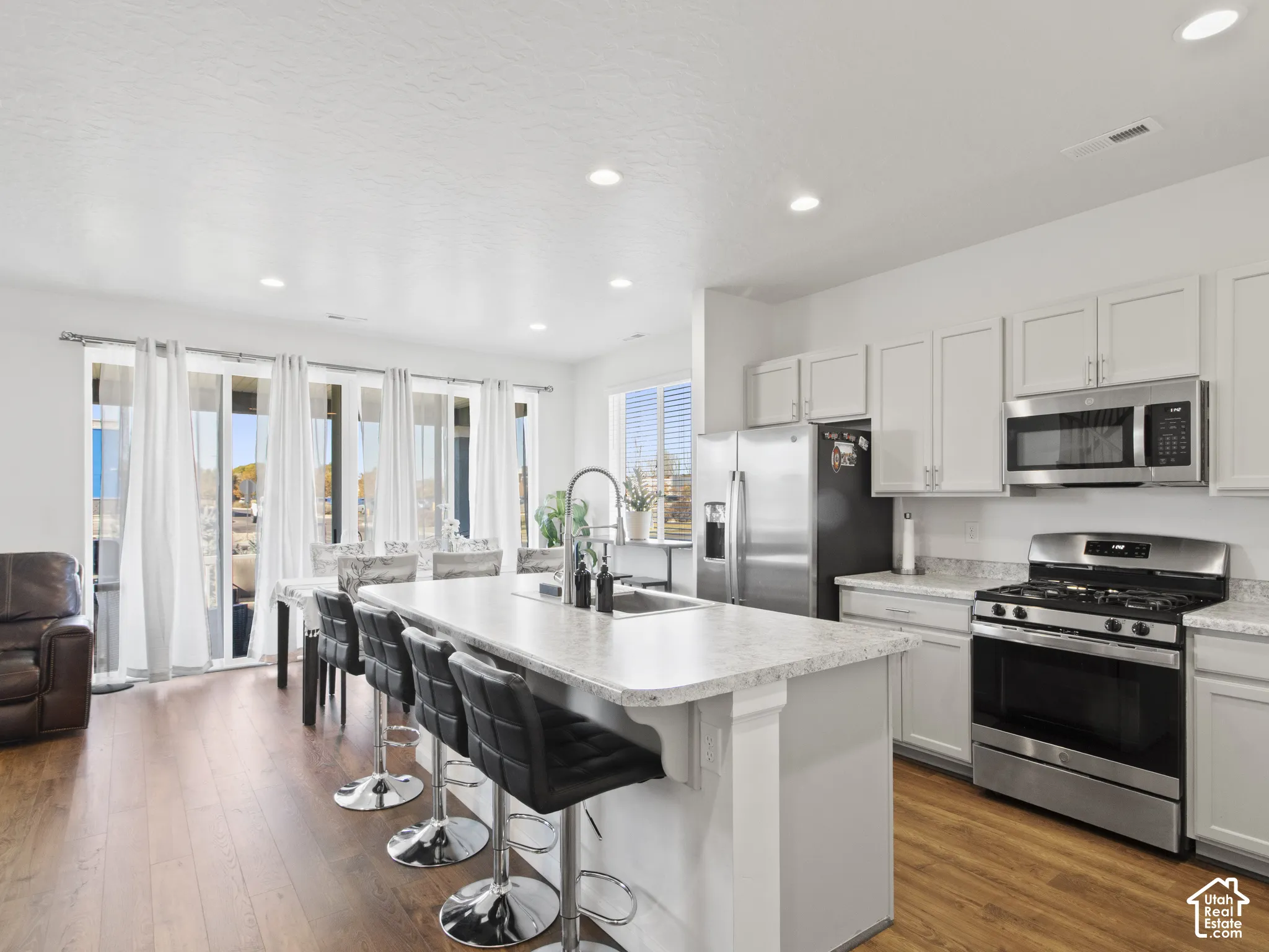 Kitchen featuring white cabinetry, stainless steel appliances, an island with seating, and wood-finish flooring