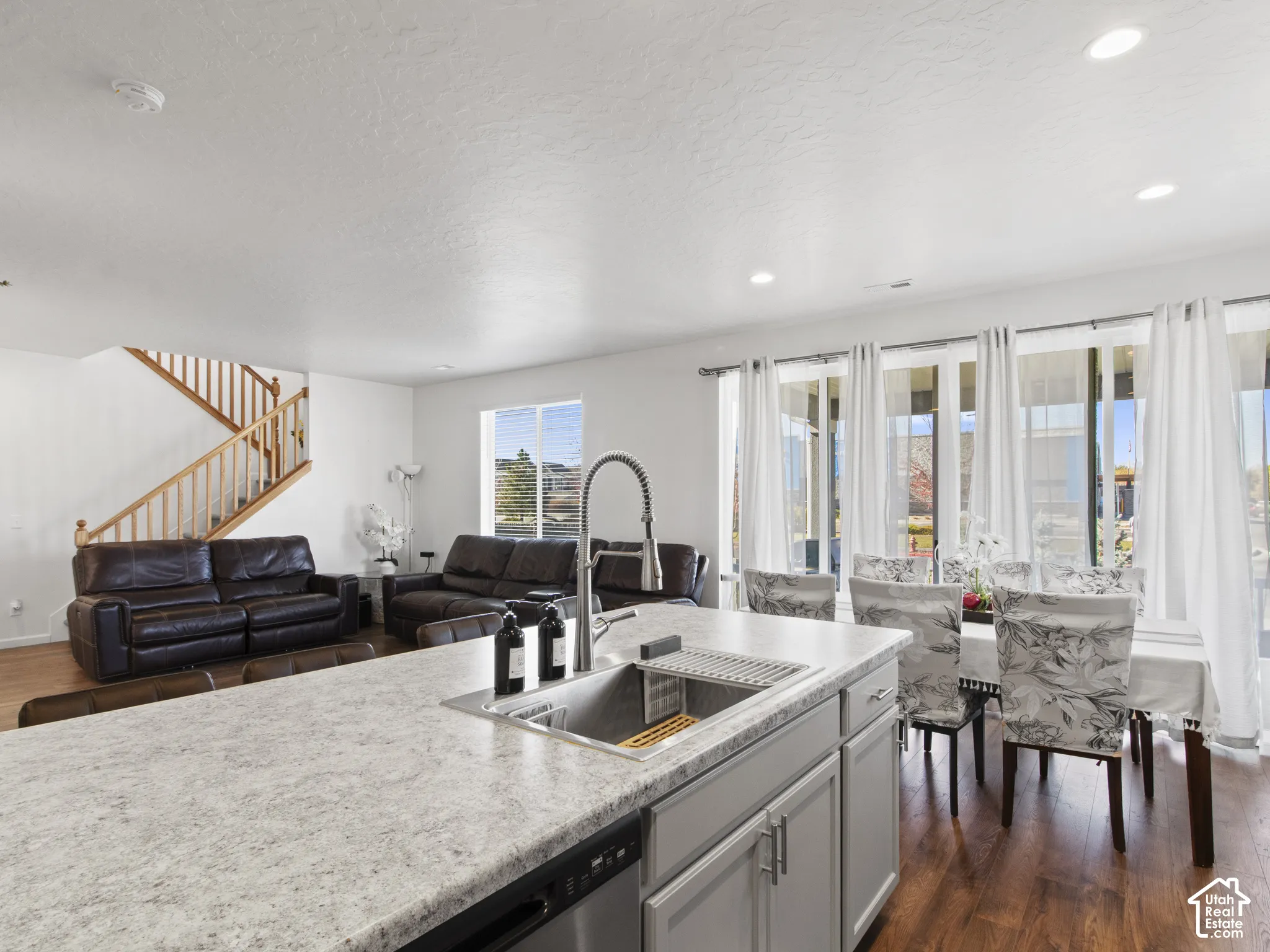 Open-concept living area featuring wood-finish flooring, a kitchen island with an integrated sink, recessed lighting, and a dining area with multiple windows