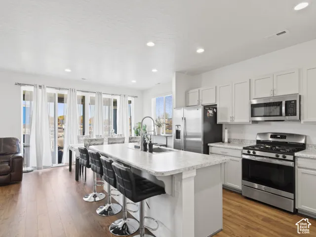 Kitchen featuring white cabinetry, stainless steel appliances, an island with seating, and wood-finish flooring