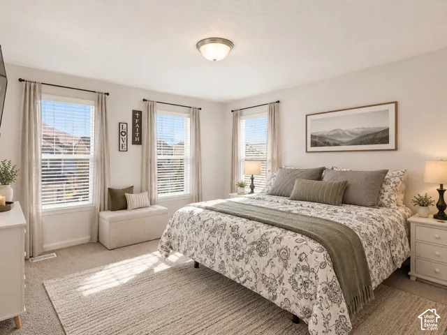 Neutral-toned bedroom featuring wall-to-wall carpeting, three windows with natural light, and a flush-mount ceiling light fixture