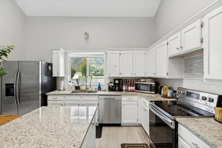 Chef's kitchen featuring white cabinetry with hardware accents, light-filled countertops with waterfall edge island, stainless steel appliances including refrigerator and range, subway tile backsplash, and abundant natural light from multiple windows over