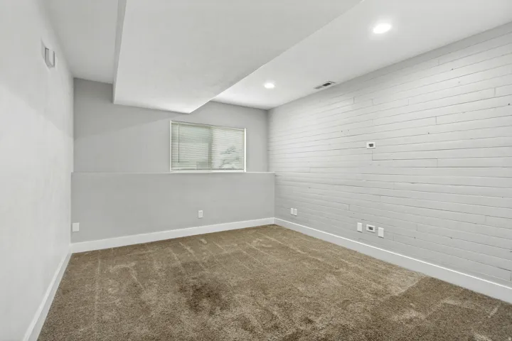 Recessed lighting, wood-finish accent wall, window with blinds, and carpeted flooring