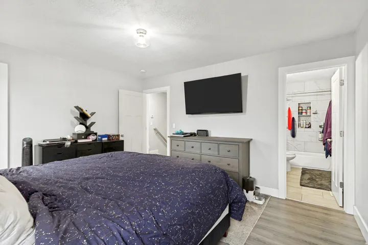 Light gray wall color, wood-finish flooring, recessed ceiling light, white interior doors, and a bathroom with a tiled shower surround