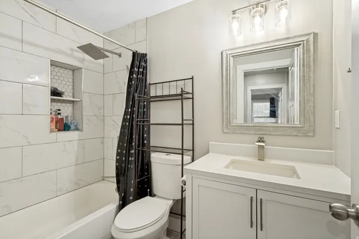 White subway tile shower surround with a built-in hexagonal tile niche, a rainfall showerhead, a single vanity with an integrated sink, and a framed mirror