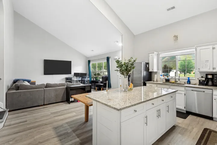 Spacious kitchen with a granite countertop island, stainless steel appliances, white cabinetry, and wood-finish flooring