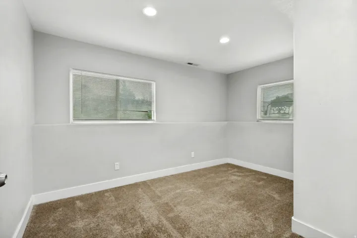 Recessed lighting, light gray walls, white trim, two windows with blinds, and brown carpeting