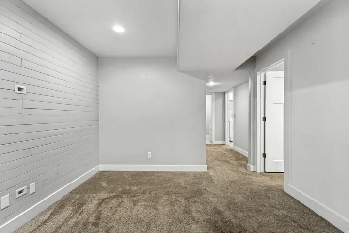 Textured accent wall, recessed lighting, neutral carpeting, white trim, and white interior doors