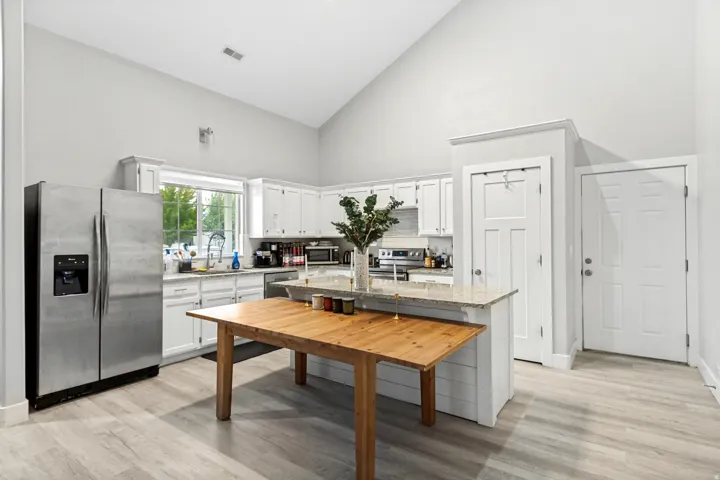 Vaulted ceiling, white shaker cabinetry, stainless steel appliances, light wood-finish flooring, and a kitchen island with seating