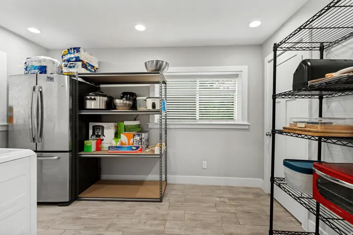 Recessed ceiling lighting, a window with blinds, wood-finish tile flooring, a stainless steel refrigerator, and built-in shelving