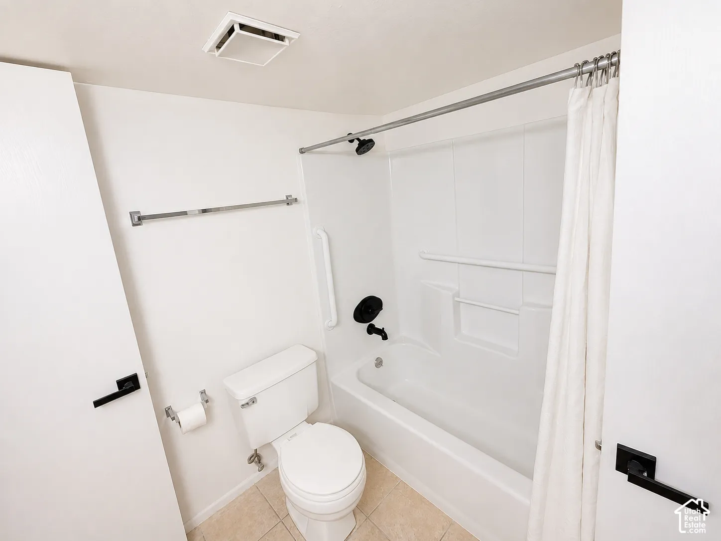 White bathtub and shower combination with matte black fixtures, integrated shelving, and a safety grab bar