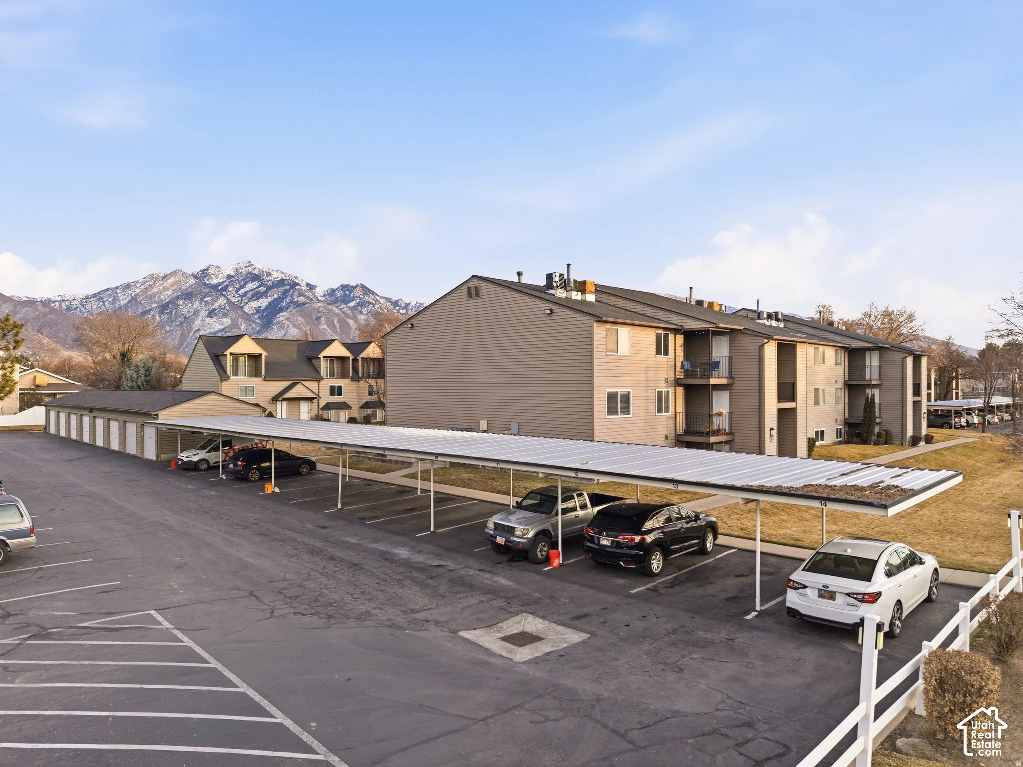 Expansive paved parking area, covered parking structures, separate garage units, multi-story residential buildings, and mountain scenery
