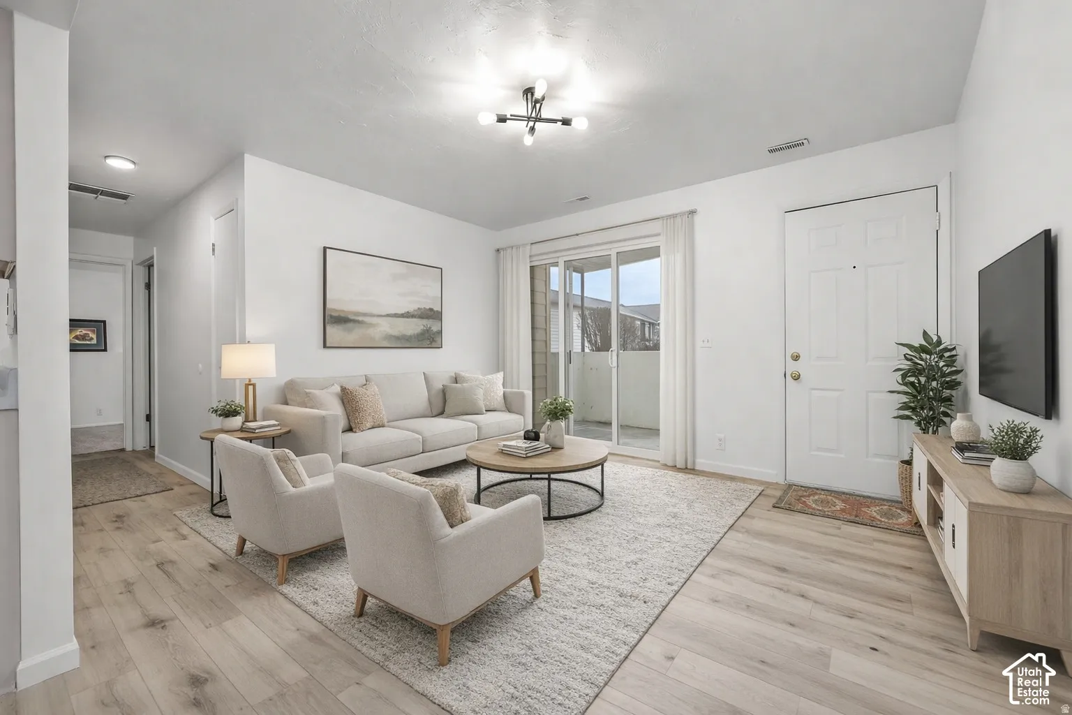 Open-concept living area featuring wood-finish flooring, a sliding glass door to an outdoor space, and a contemporary ceiling light fixture