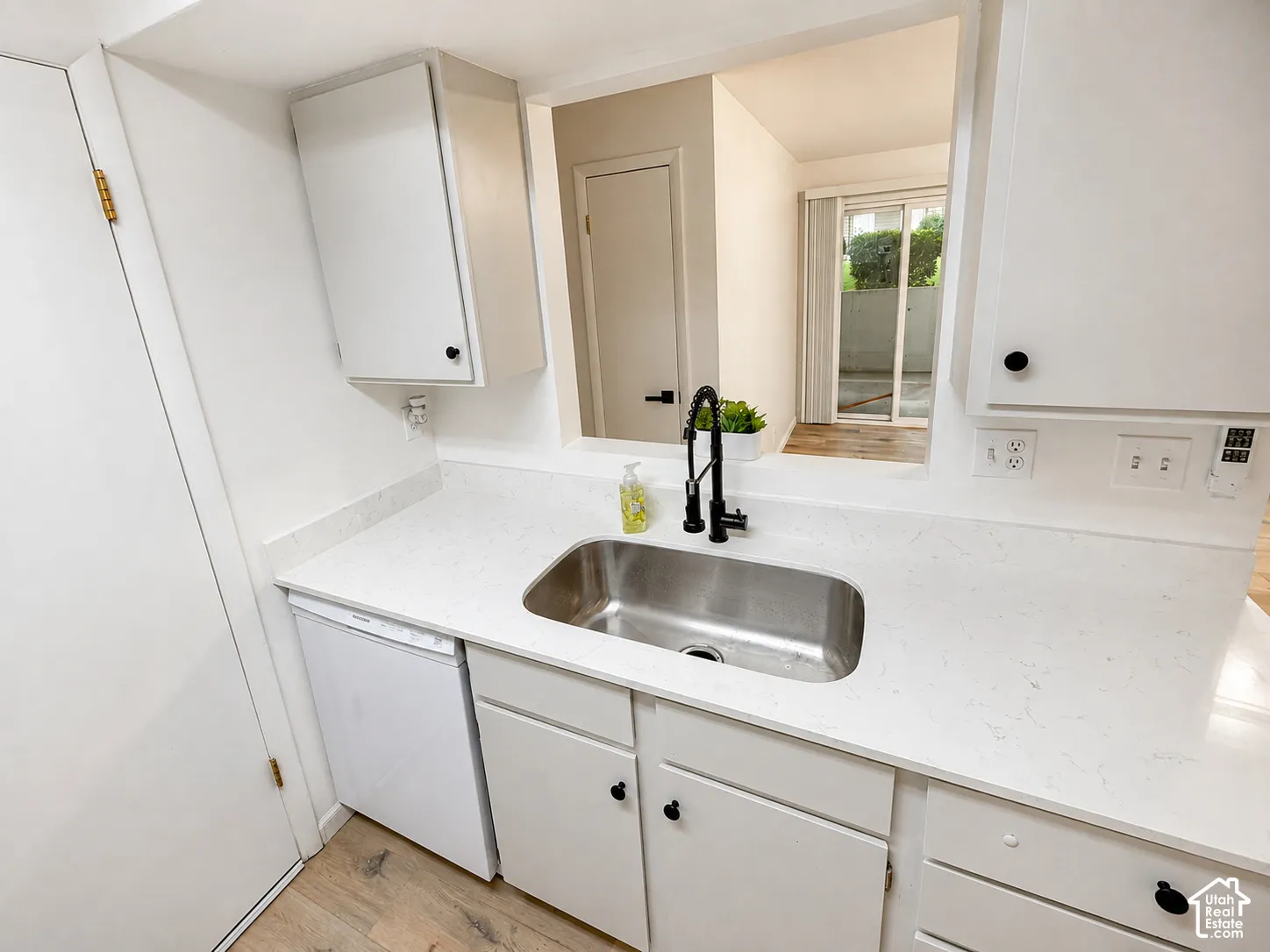White cabinetry with matte black hardware, stainless steel sink, white countertop, black pull-down faucet, and wood-finish flooring