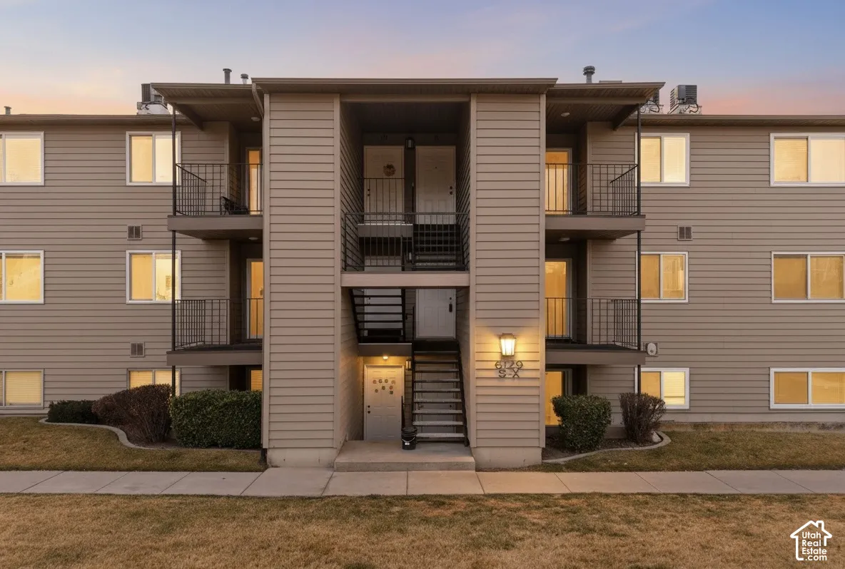 Multi-story building with horizontal siding, exterior balconies with metal railings, outdoor stair access, and foundational landscaping