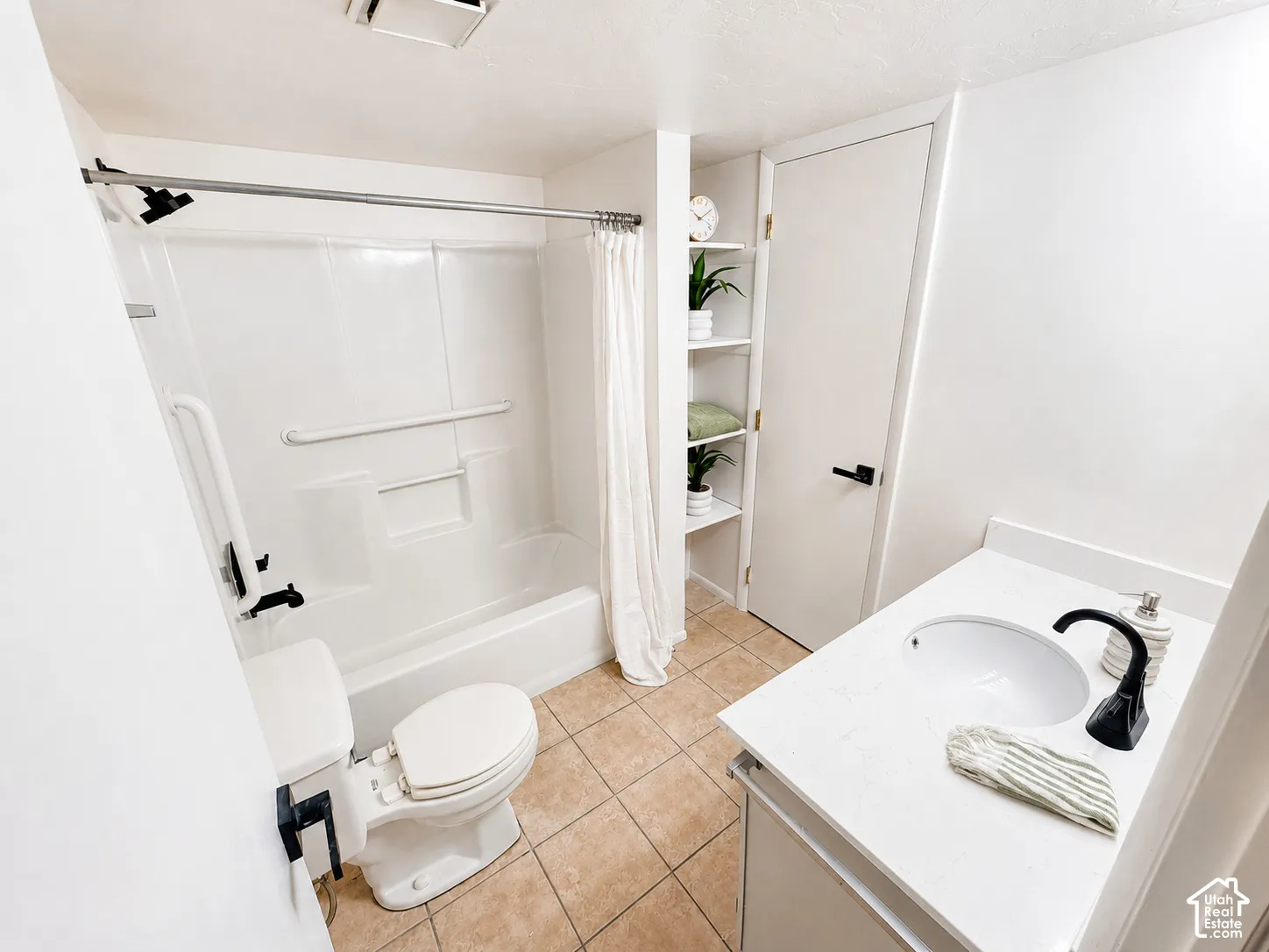 White vanity with a single basin sink and a matte black faucet, white shower/tub combination with grab bars, toilet with a bidet attachment, and built-in shelving
