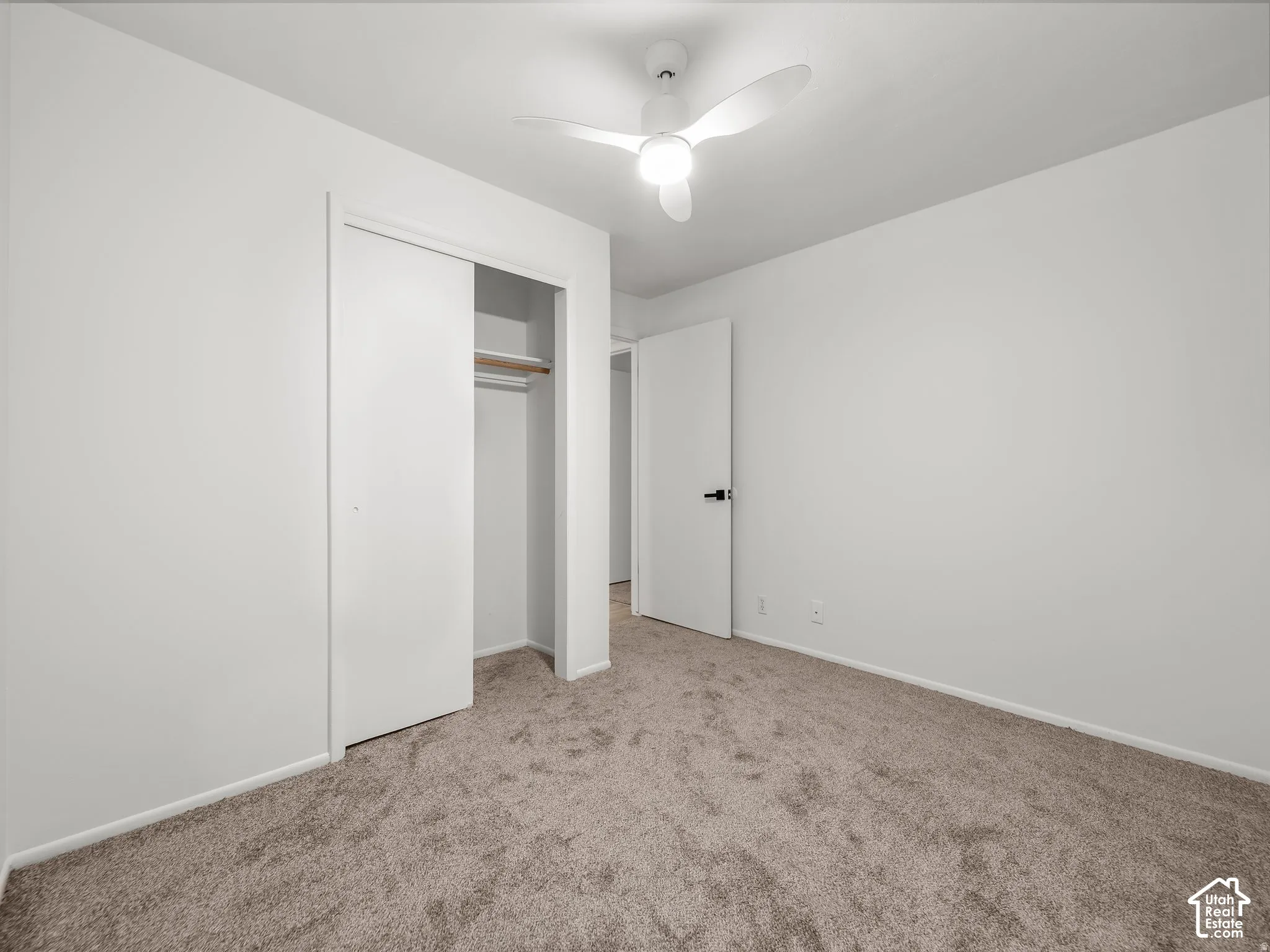 Neutral toned carpeting, contemporary ceiling fan, white walls, and a built-in closet with sliding doors
