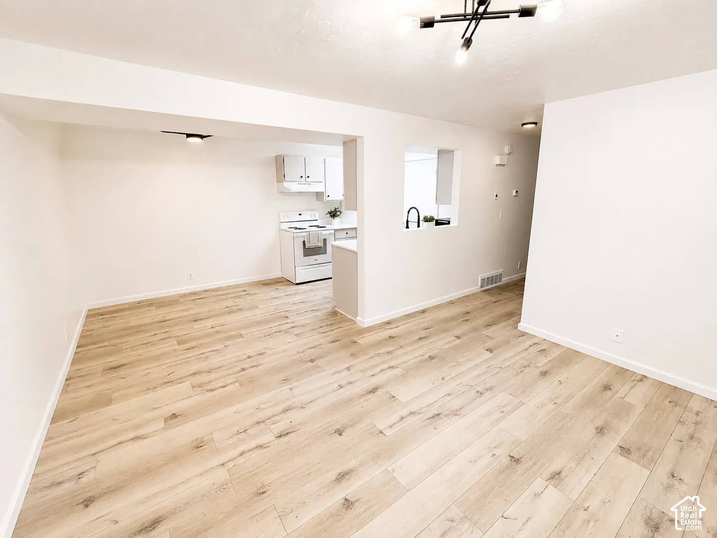 Expansive open-concept living space with light wood-finish flooring, white walls, and a modern ceiling fixture