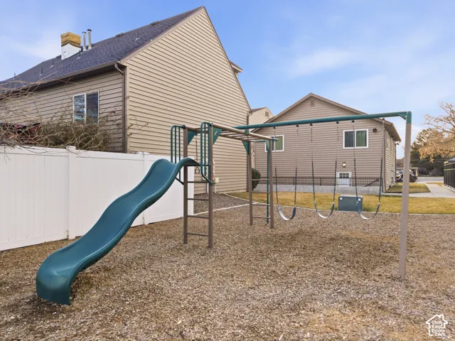 Fenced backyard with playground equipment including a slide and monkey bars, situated on a gravel surface